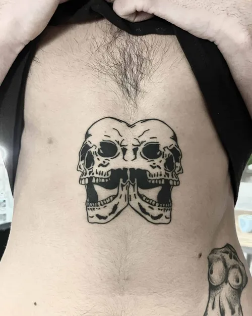 Blackwork tattoo of two joined skulls on a torso